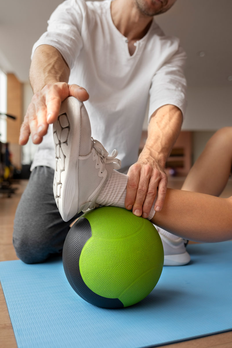 Ein Fussgelenk wird von einem Physiotherapeuten einfühlsam auf einem therapeutischen Ball gedehnt.